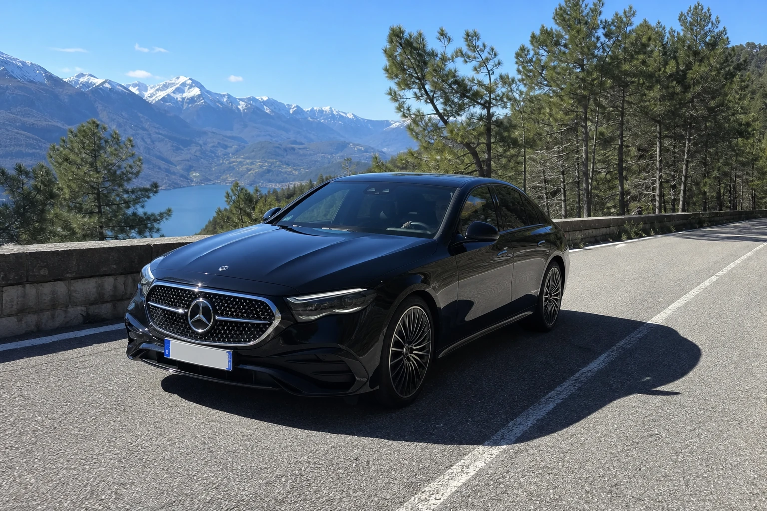 Mercedes Classe E noire sur une route alpine surplombant un lac, en direction de Milan, chauffeur privé BSM