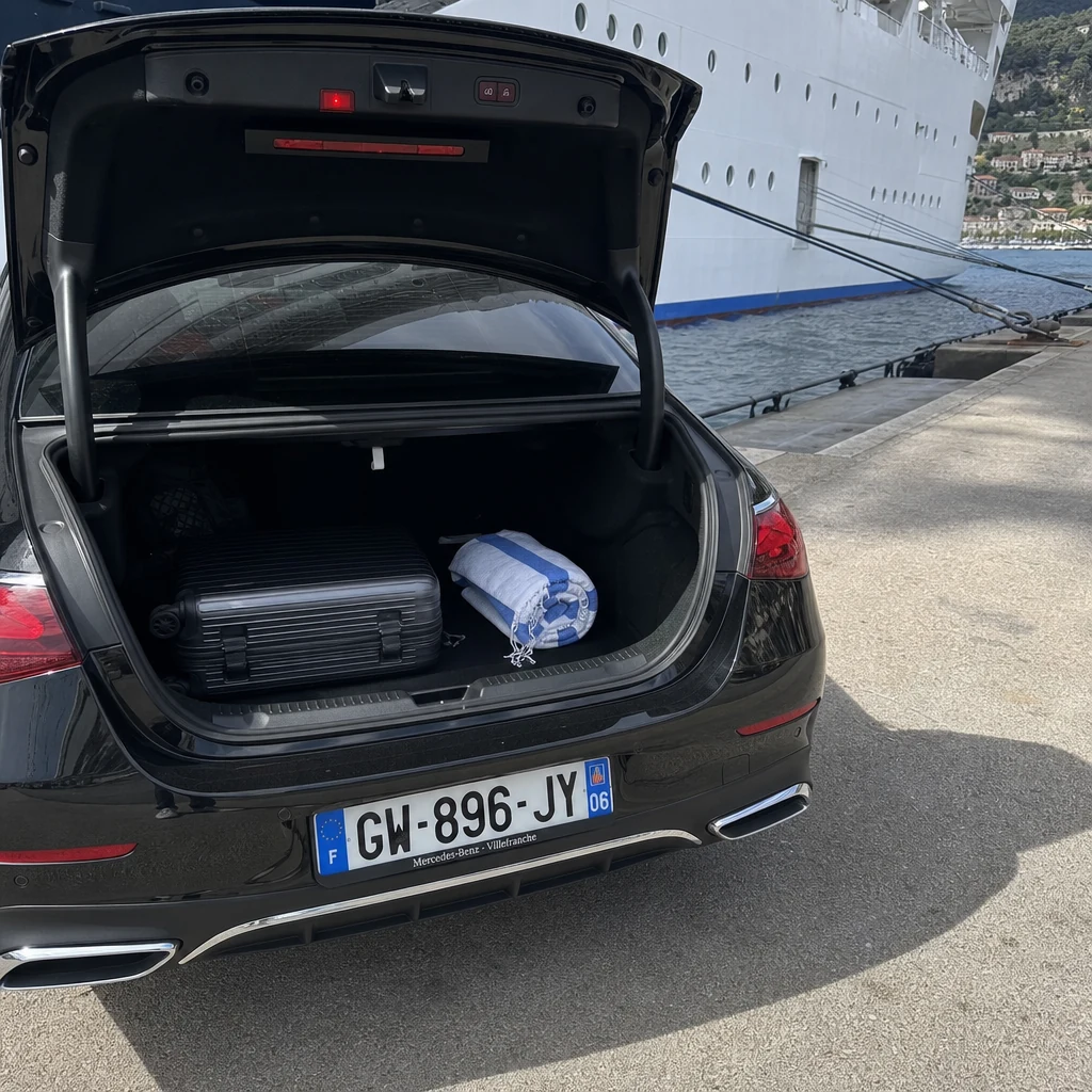 Coffre ouvert d'une Mercedes Classe E noire sur le quai du port de Villefranche-sur-Mer, coque de paquebot de croisière en arrière-plan — chauffeur pour excursions croisière